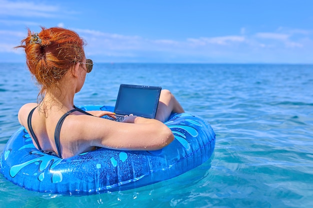 Concetto di lavoro a distanza. Donna di affari che si siede in un anello gonfiabile in mare