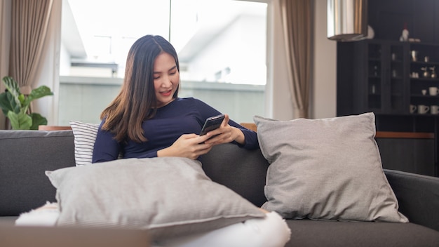 Concetto di lavoro da casa una giovane donna d'affari seduta su un comodo divano usando il suo telefono cellulare in chat con i clienti.