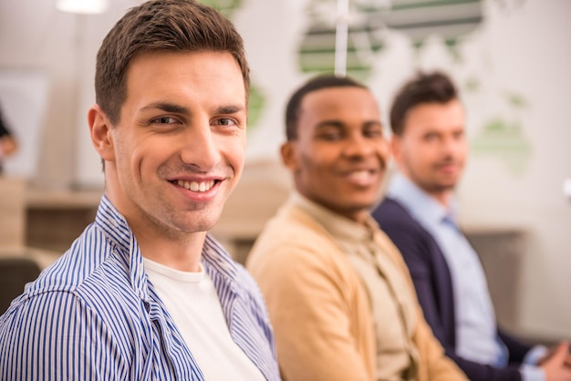 Concetto di lavoro di squadra I giovani sono seduti in ufficio a lavorare e guardano la telecamera