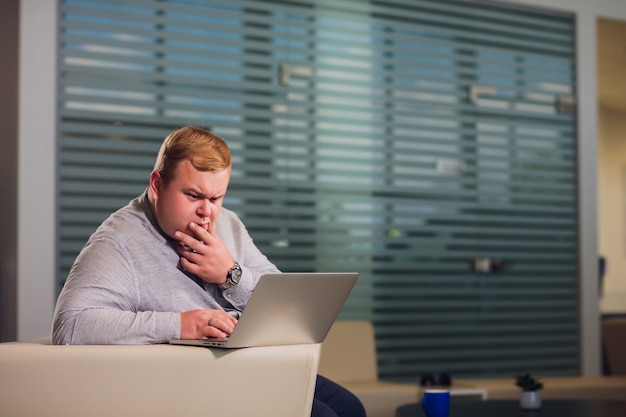 Concetto di lavoro in ufficio. L'uomo sta navigando sul suo computer portatile, seduto in ufficio sul comodo divano bianco