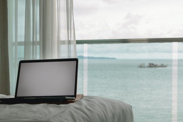 Concetto di lavoro laptop schermo vuoto sul letto e balcone con vista sull'oceano