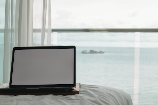 Concetto di lavoro laptop schermo vuoto sul letto e balcone con vista sull'oceano