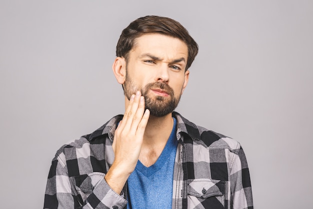 Concetto di mal di denti. Tiro al coperto di giovane sensazione di dolore, tenendo la guancia con la mano, soffre di mal di denti male isolato su muro grigio.