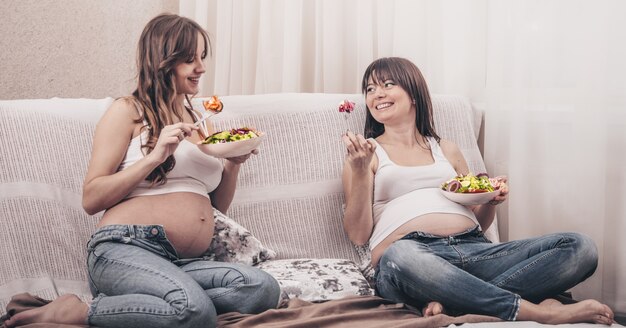 Concetto di maternità, due donne incinte che mangiano insalata fresca a casa