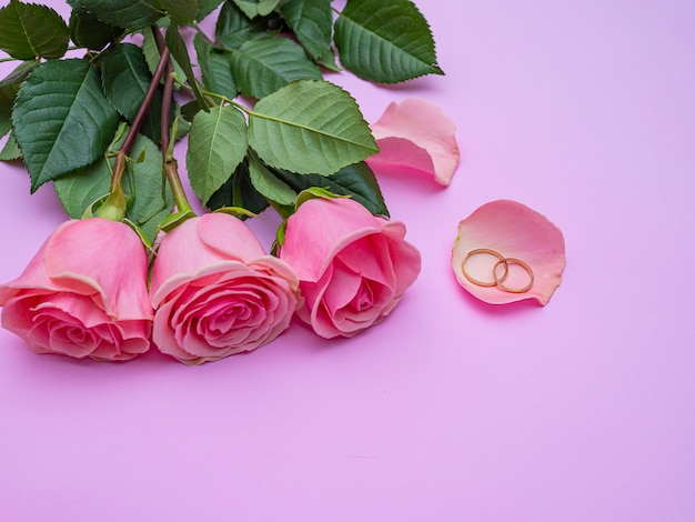 Concetto di matrimonio. Bella rosa rosa su sfondo rosa con due anelli di nozze. Copia spazio.