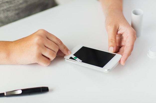 concetto di medicina, diabete, glicemia, assistenza sanitaria e persone - primo piano delle mani della donna con smartphone che controlla il livello di zucchero nel sangue tramite glucometro a casa