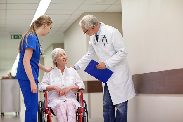 concetto di medicina, età, assistenza sanitaria e persone - medico, infermiere e paziente anziano in sedia a rotelle nel corridoio dell'ospedale
