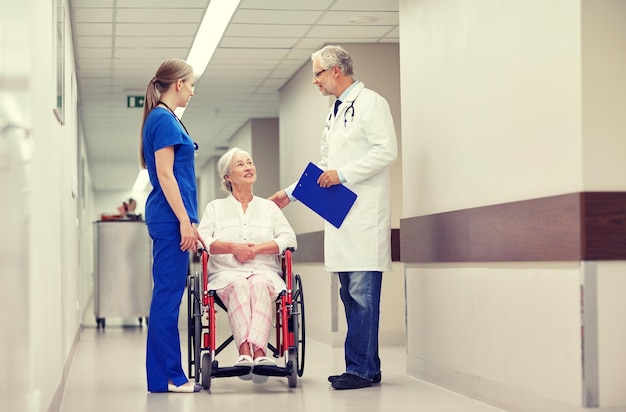 concetto di medicina, età, assistenza sanitaria e persone - medico, infermiere e paziente anziano in sedia a rotelle nel corridoio dell'ospedale