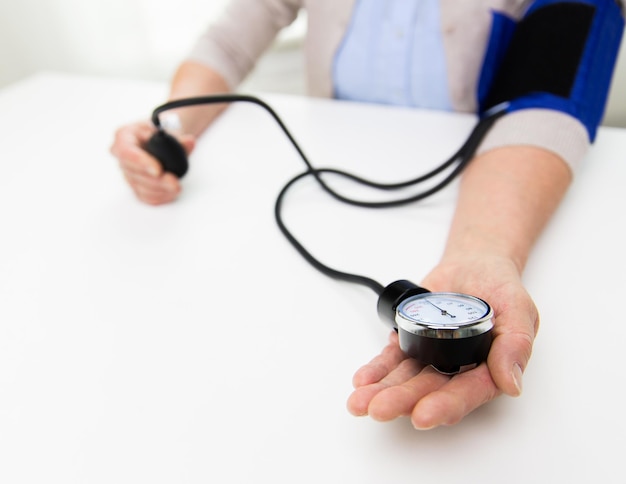 concetto di medicina, età, assistenza sanitaria e persone - primo piano di donna anziana con tonometro che controlla il livello di pressione sanguigna a casa