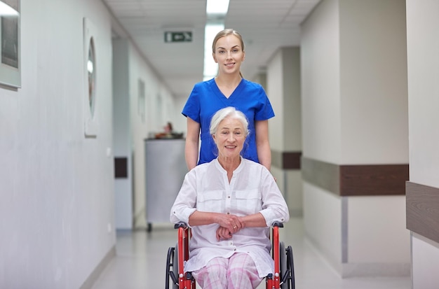 concetto di medicina, età, supporto, assistenza sanitaria e persone - infermiera che prende un paziente anziano in sedia a rotelle nel corridoio dell'ospedale