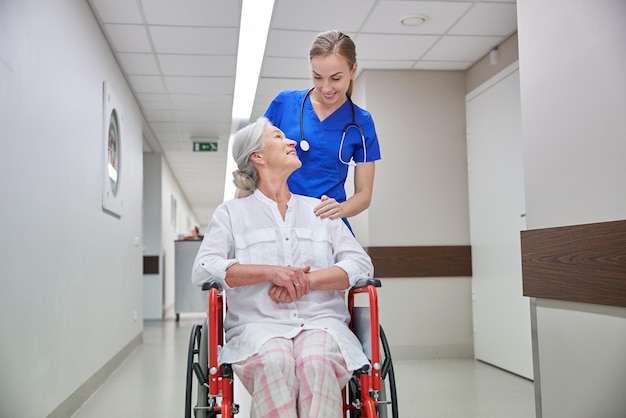 concetto di medicina, età, supporto, assistenza sanitaria e persone - infermiera felice che prende un paziente anziano in sedia a rotelle nel corridoio dell'ospedale