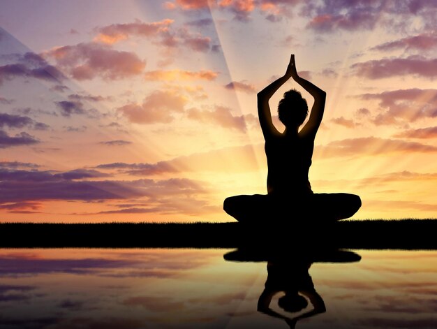 Concetto di meditazione e rilassamento. Siluetta di una ragazza che pratica yoga al tramonto e riflesso nell'acqua