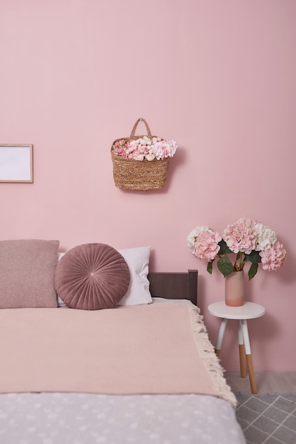 Concetto di mobili camera da letto interna. Accogliente angolo camera da letto rosa. Accogliente camera da letto femminile con letto rosa, cuscini decorativi e pianta su uno sgabello in legno.