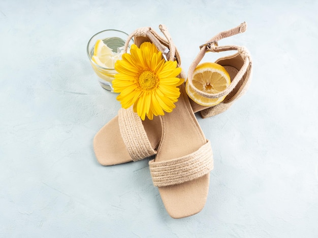 Concetto di moda estiva con sandali di paglia su sfondo turchese con fiori gialli e limoni