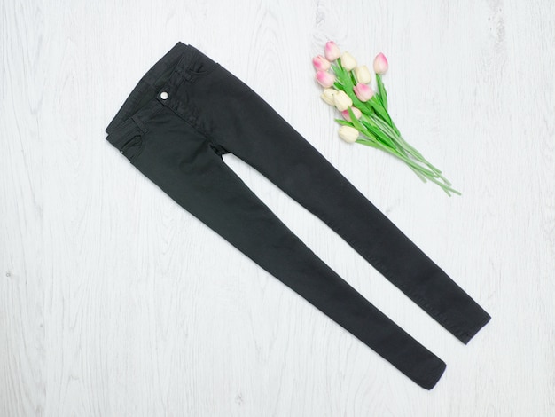 Concetto di moda. Jeans neri e tulipani rosa. Sfondo di legno