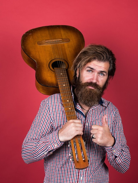 Concetto di musica. brutale bell'uomo con i baffi suona la chitarra. musicista e cantante maturo. chitarrista dallo stile casual. hipster barbuto dall'aspetto moderno con chitarra acustica.