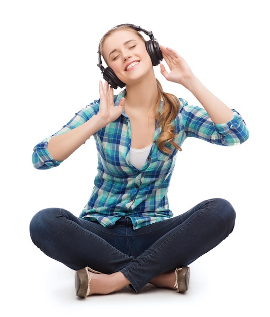 concetto di musica e tecnologia - giovane donna sorridente seduta sul pavimento e ascoltando musica con le cuffie