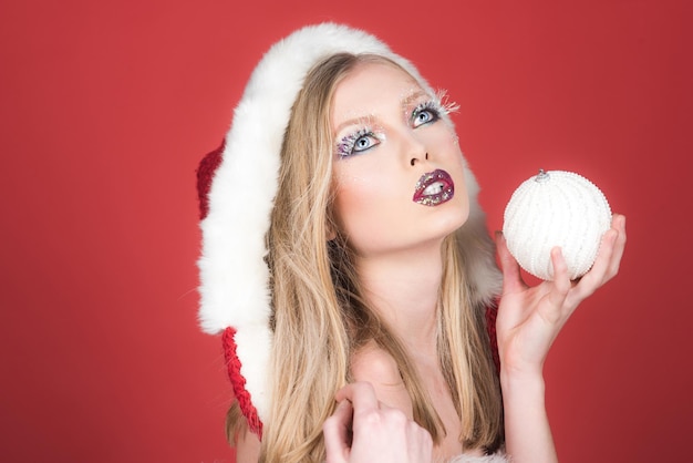 Concetto di Natale, Capodanno, inverno, vacanza, festa e celebrazione - una donna attraente con il cappello da Babbo Natale tiene in mano il giocattolo di Capodanno. Trucco festivo luminoso.