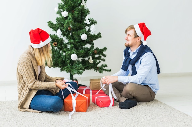Concetto di Natale e festività - Giovani coppie felici che indossano cappelli di Babbo Natale che aprono i regali a casa.