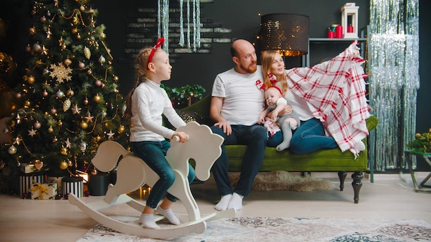 Concetto di Natale famiglia felice che si rilassa sul divano in soggiorno figlia che gioca sul cavallo giocattolo