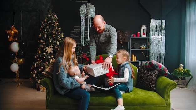 Concetto di Natale famiglia seduta sul divano papà che dà agli altri un regalo