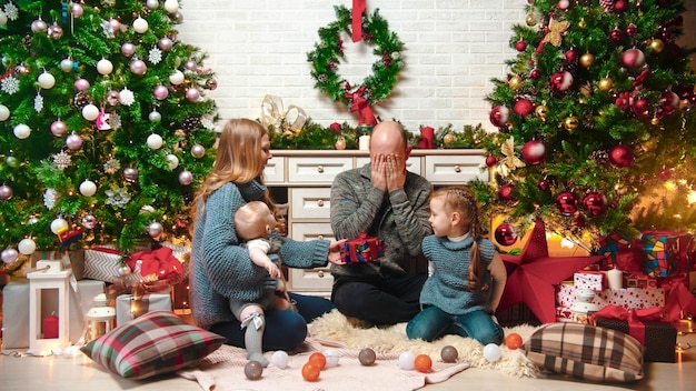 Concetto di Natale felice famiglia di successo siede nell'ambiente natalizio e scambia regali papà seduto con gli occhi chiusi