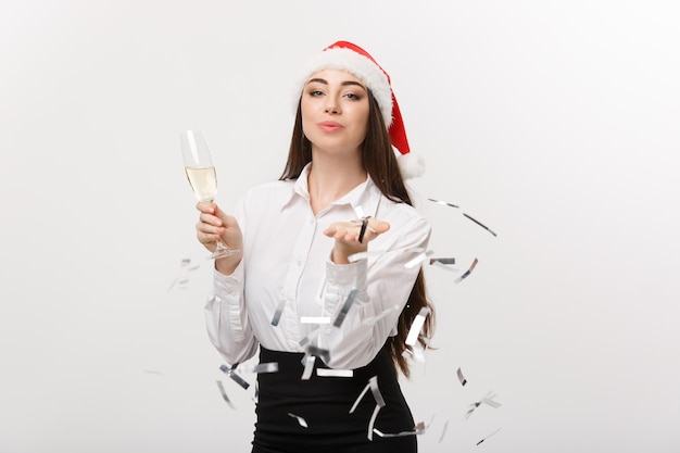 Concetto di Natale giovane donna d'affari in possesso di champagne e soffiando coriandoli