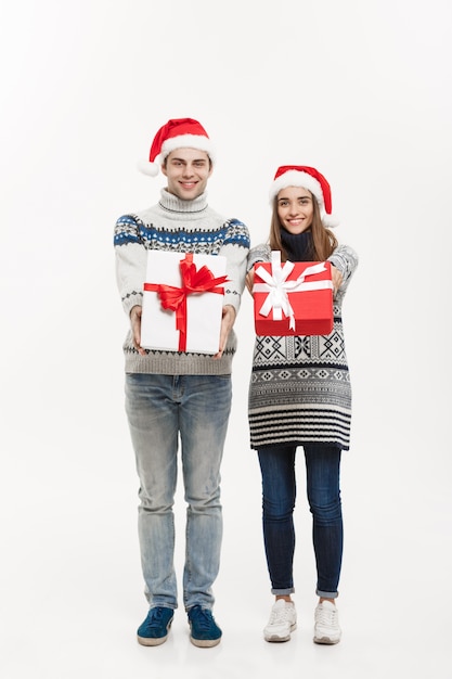 Concetto di Natale - giovani regali adorabili della tenuta delle coppie isolati su fondo grigio bianco.