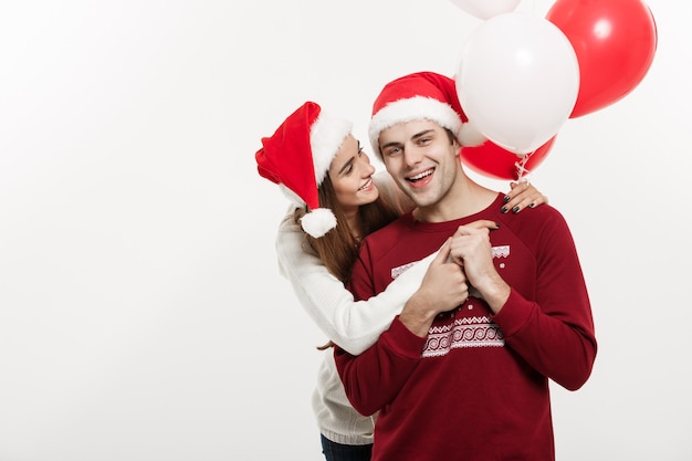 Concetto di Natale - Il palloncino della holding della giovane ragazza sta abbracciando e giocando con il suo ragazzo facendo una sorpresa a Natale.