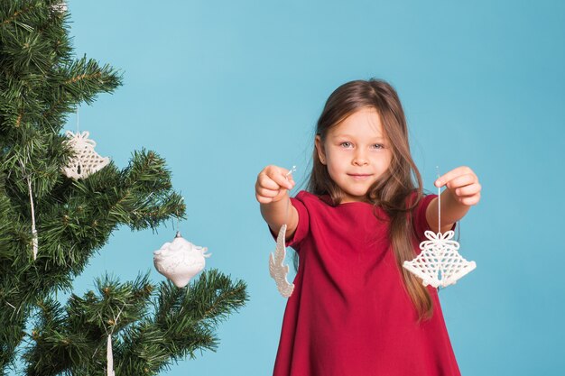 Concetto di Natale, infanzia e persone - bambina che decora l'albero di Natale