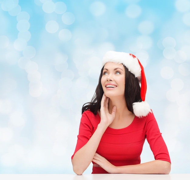 concetto di natale, inverno, vacanze, felicità e persone - donna sorridente in cappello di Babbo Natale su sfondo di luci blu