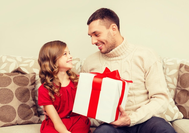 concetto di natale, natale, inverno, felicità e persone - padre e figlia sorridenti che tengono una confezione regalo e si guardano l'un l'altro