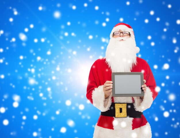 concetto di natale, pubblicità, tecnologia e persone - uomo in costume di babbo natale con computer tablet pc su sfondo blu innevato