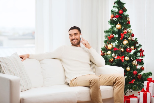 concetto di natale, tecnologia, persone e vacanze - uomo sorridente che chiama smartphone a casa