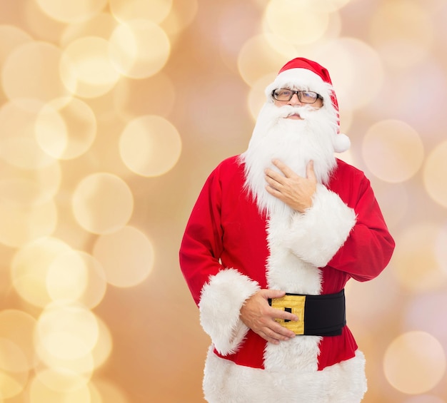 concetto di natale, vacanze e persone - uomo in costume di babbo natale su sfondo di luci beige