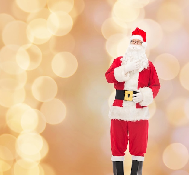 concetto di natale, vacanze e persone - uomo in costume di babbo natale su sfondo di luci beige