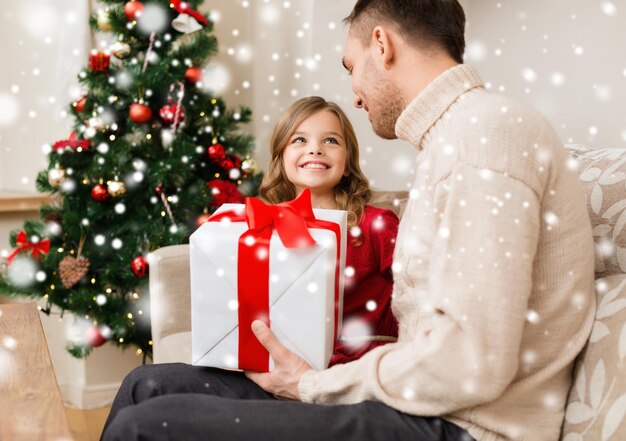 concetto di natale, vacanze, famiglia e persone - padre e figlia sorridenti che tengono scatola regalo a casa