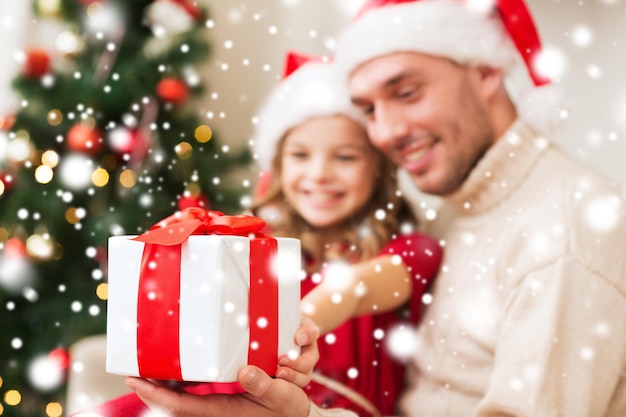 concetto di natale, vacanze, famiglia e persone - padre e figlia sorridenti che tengono una confezione regalo e si abbracciano a casa