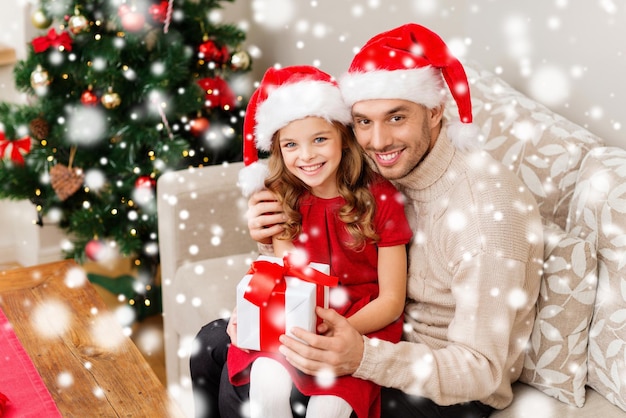 concetto di natale, vacanze, famiglia e persone - padre e figlia sorridenti che tengono una confezione regalo e si abbracciano a casa