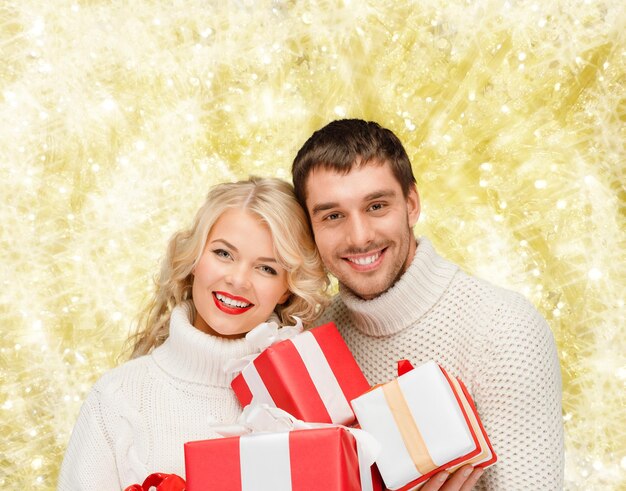 concetto di natale, vacanze, felicità e persone - uomo e donna sorridente con regali su sfondo di luci gialle