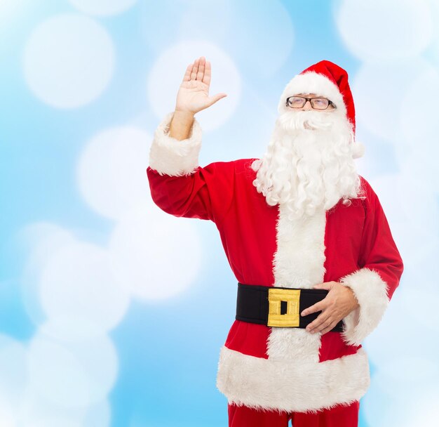 concetto di natale, vacanze, gesto e persone - uomo in costume di babbo natale che agita la mano su sfondo di luci blu