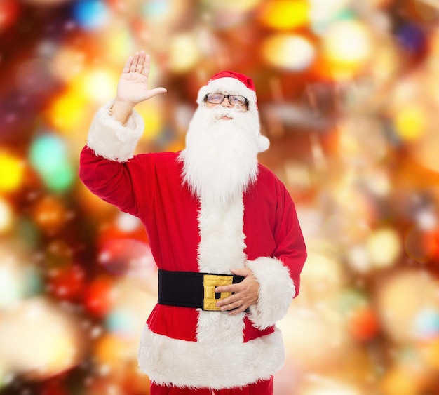 concetto di natale, vacanze, gesto e persone - uomo in costume di babbo natale che agita la mano su uno sfondo di luci rosse