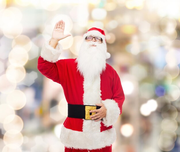 concetto di natale, vacanze, gesto e persone - uomo in costume di babbo natale che agita la mano sullo sfondo delle luci