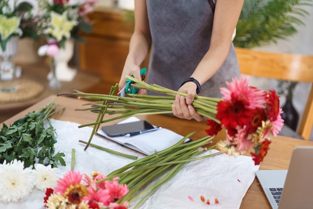 Concetto di negozio di fiori Il fiorista femminile sta tagliando steli di gerbera con le forbici per fare mazzi di fiori