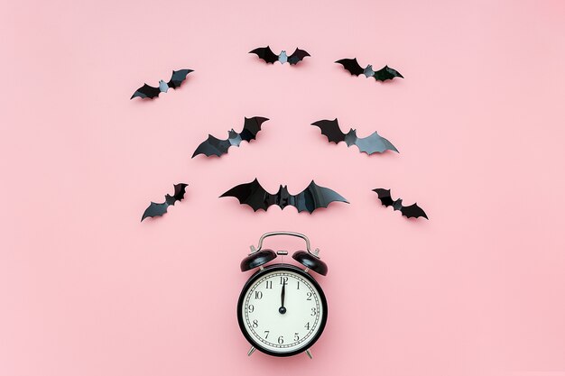 Concetto di notte di Halloween. Sveglia nera e pipistrelli volanti sul rosa