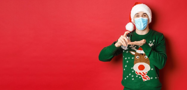 Concetto di nuovo anno coronavirus e distanziamento sociale giovane attraente con maschera medica con cappello da Babbo Natale...