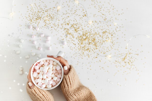 Concetto di nuovo anno. Tazza con cioccolata calda e marshmallow in mano su uno sfondo bianco