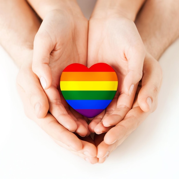 concetto di orgoglio gay, omosessuale, amore e carità - primo piano di mani maschili e femminili che tengono un piccolo cuore arcobaleno