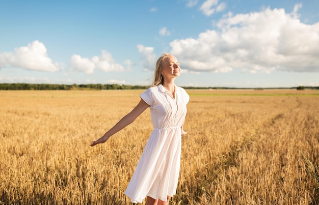 concetto di paese, natura, vacanze estive, vacanza e persone - giovane donna sorridente in abito bianco sul campo di cereali