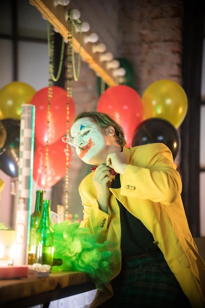 Concetto di pagliaccio un clown uomo perso in giacca gialla che fuma una sigaretta e si toglie un papillon